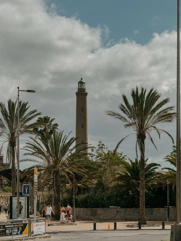 Il faro di Maspalomas tra le palme, visto dalla strada con cartelli e pubblicità immobiliari